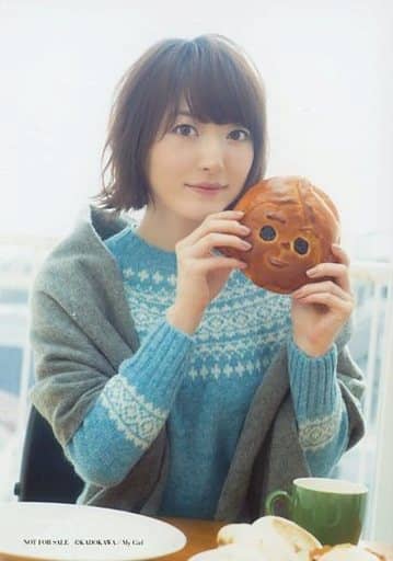 Hanazawa Kana in a blue crochet top donning a gray jacket, holding a piece of bread of a face with eyes as holes