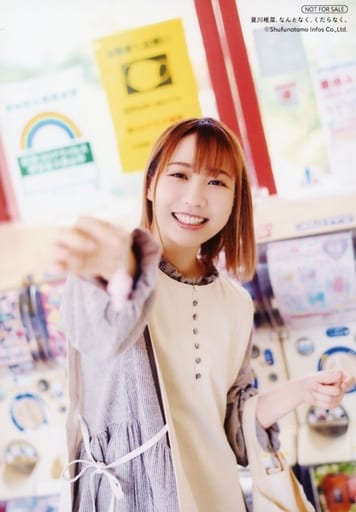 Natsukawa Shiina in front of a bunch of capsule toy machines, dressed in casual clothing with a shopping bag hanging on her left hand, her right hand holding out a keychain