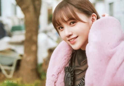 Kitou Akari dressed in a black blouse and pink coat, standing by a tree in the background