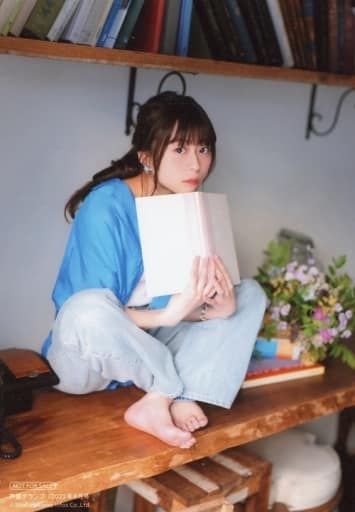 Minase Inori sitting on a wooden table holding on to a white covered book with its inner binder against her chin