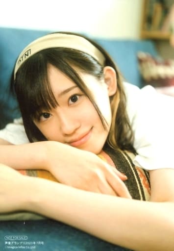 Takahashi Rie dressed in a white T-shirt with a yellow headband, laying prone on a cyan-coloured sofa